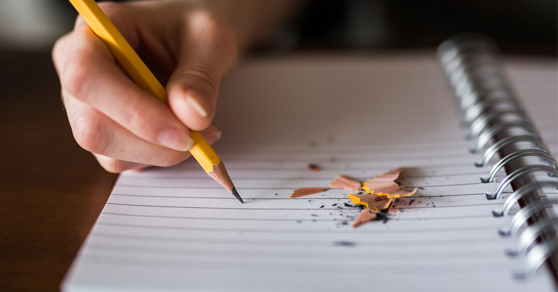 person using pencil to write on paper covered with pencil shavings