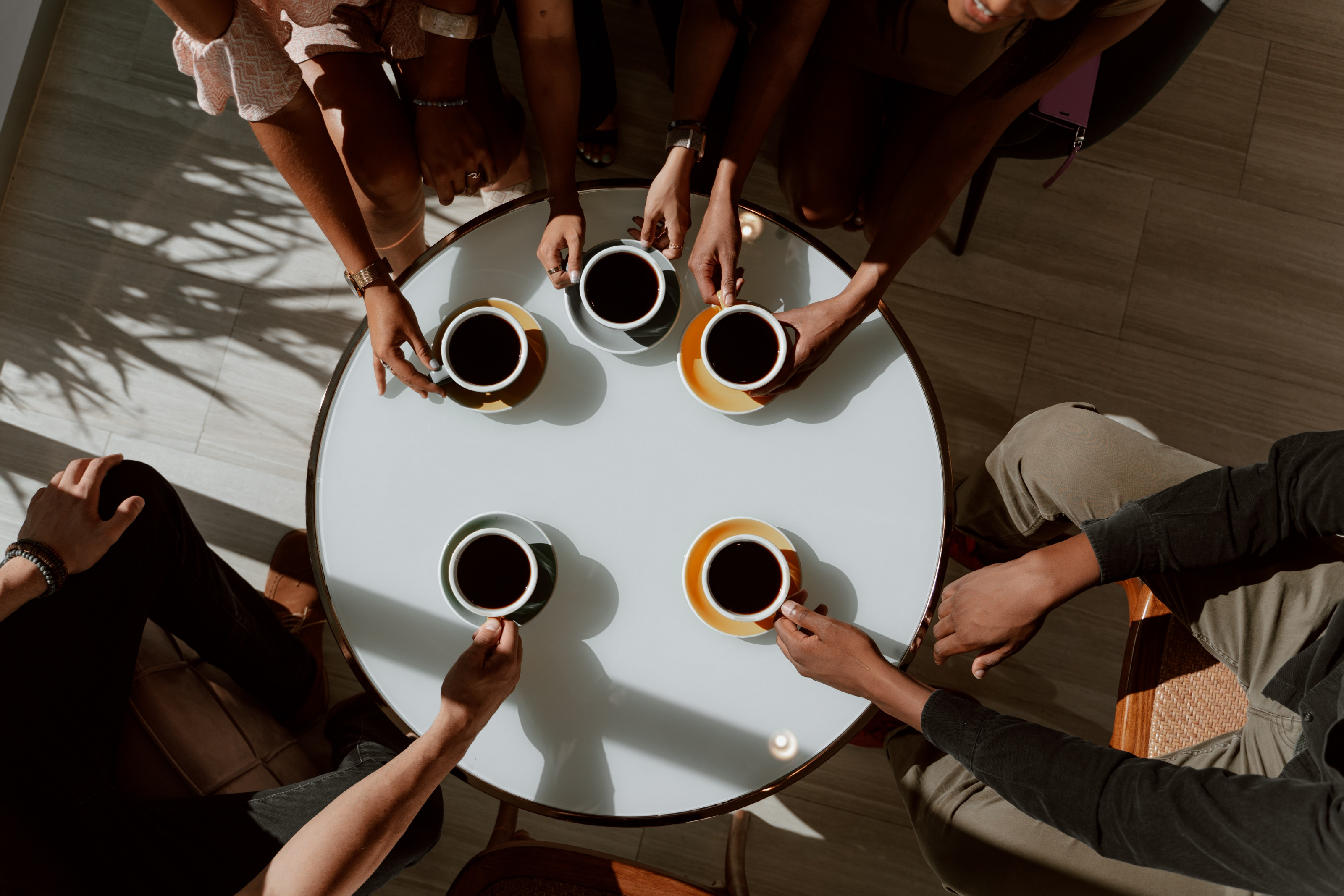 Five people around a table each holding a cup of coffee.