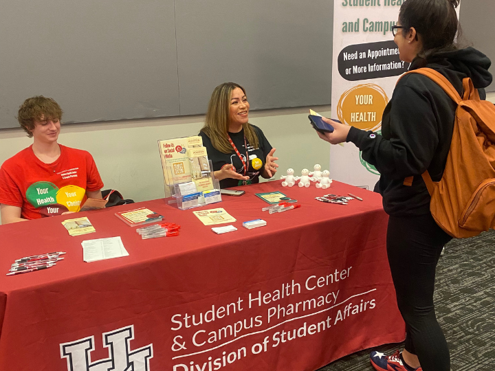 Woman
sitting
inside
at
a
table
with
another
staff
member
talking
with
a
UH
student
about
campus
resources.