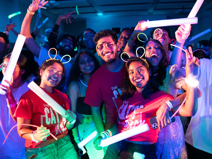3 students smiling at the camera holding glow sticks at event and having fun