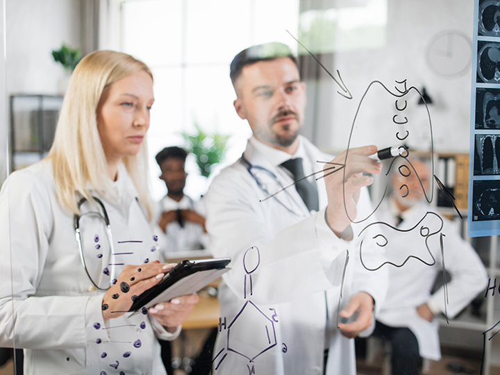Team of qualified medical scientists using tablet and writing on glass flip chart during meeting at hospital room. Clinical studies and cooperation concept.