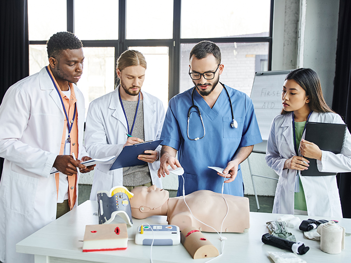 cardiac resuscitation, medical instructor holding defibrillator pads above CPR manikin near young