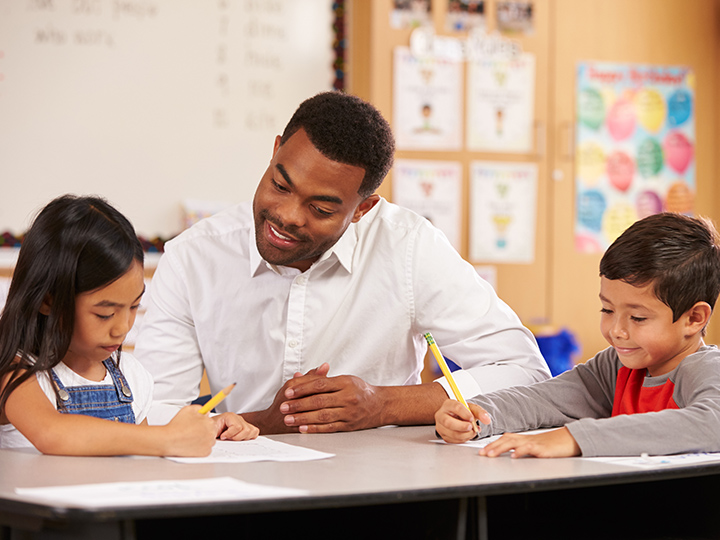 Teacher sitting at desk with two elementary school pupils
