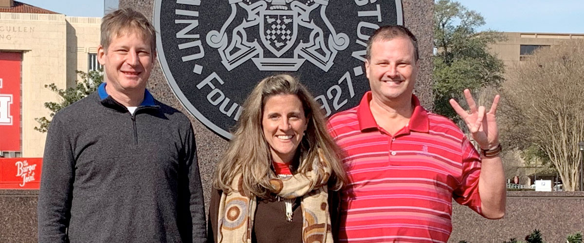 Dr. Sommers, Helena and David Seiver standing in front of UH seal emblem 