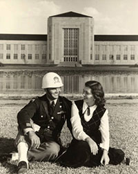 A man in a Cullen Rifles uniform sits with a woman in front of the Ezekiel Cullen Building.