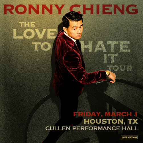 Ronnie Chieng stands on some stairs in a red velvet suit, with his arm propped on the rail. . 