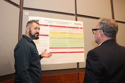 A man standing in front of a research poster on the left and a man looking at the poster on the right