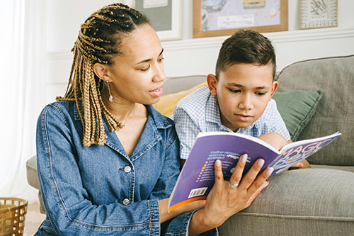 A woman with long braided hair and a blue denim shirt reading to a young boy with short brown hair