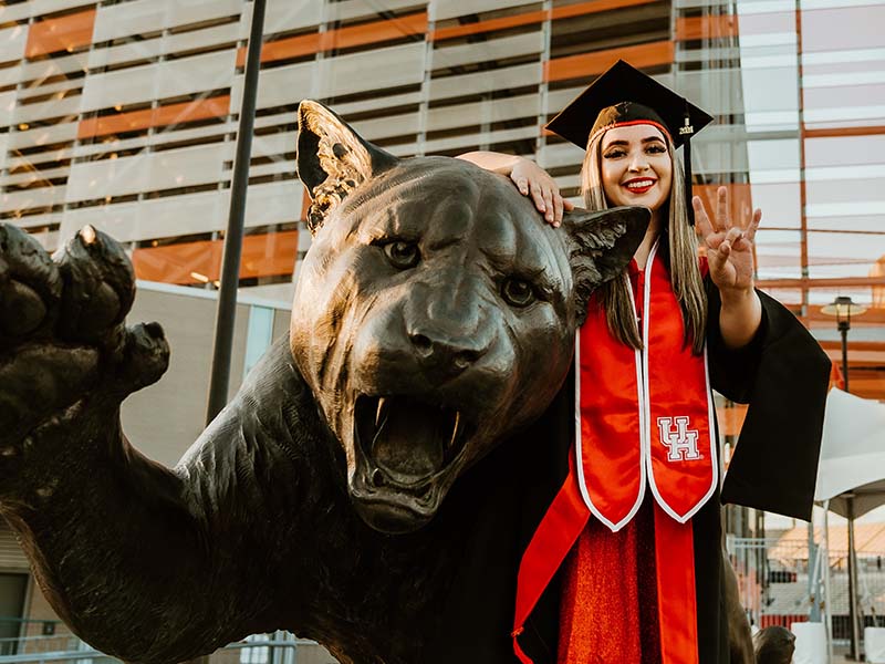 UH graduate posing for a photo with the cougar statue outside TDECU Stadium