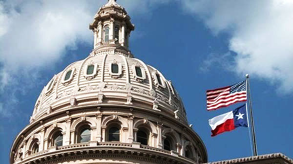 photo of the top of the Texas Capitol with the United States flag and Texas flag
