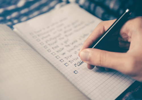 Image of a person's hand holding a pen and writing a to-do list