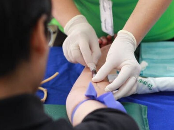 Close up of a nurse wearing latex gloves and injecting a syringe another person's arm.