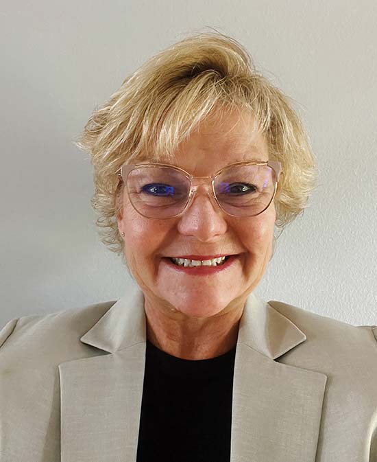 Portrait of a white woman with blonde short hair wearing glasses and a business jacket