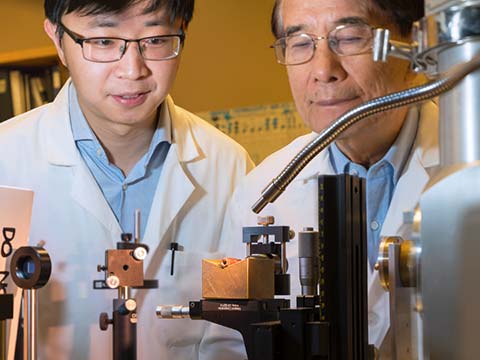 Two Asian scientists observe a mini-diamond anvil cell surrounded by lab equipment.