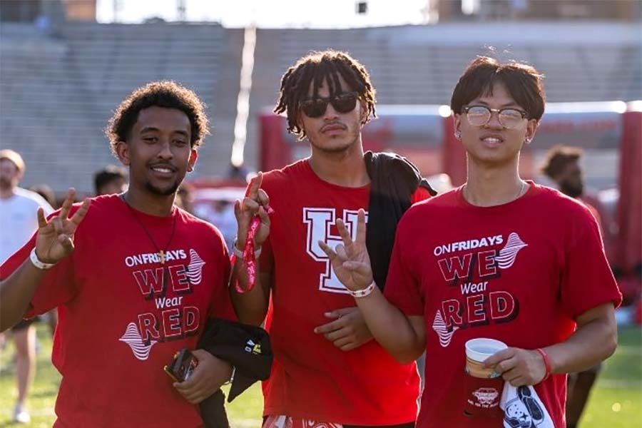 Three male students wearing red UH shirts each holding their right hand in the UH cougar paw gesture.