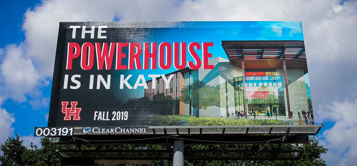 Photo of a billboard featuring a colorful rendering of a building. The words "The Powerhouse is in Katy. UH Fall 2019" are superimposed over the rendering.