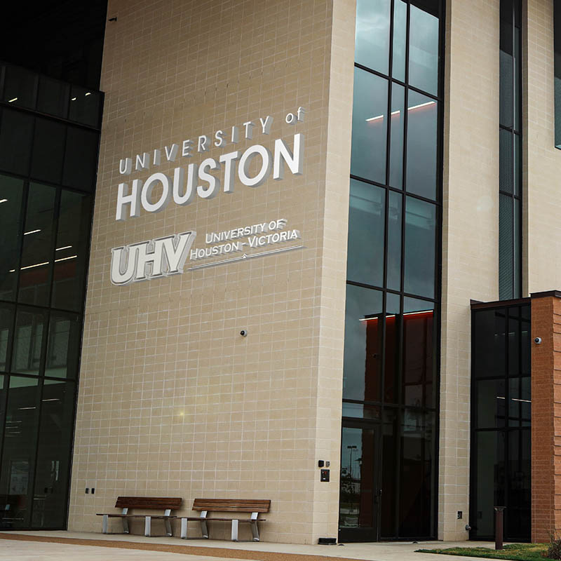 Photograph of a tall tan brick wall. Logos for the University of Houston and University of Houston - Victoria are visible.