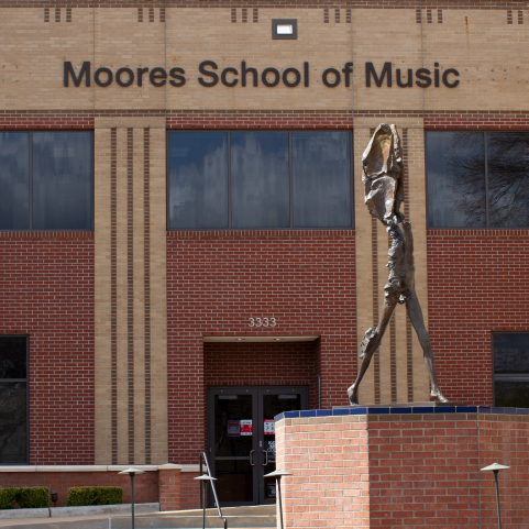 A red and tan brick building entryway with “Moores School of Music” at the top. In the foreground is a life-sized bronze figurine on a brick pedestal.