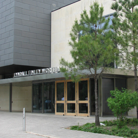 A grey and cream building with the words “Lyndall Finley Wortham Theater” atop a metal awning that covers wooden doors at the entrance.
