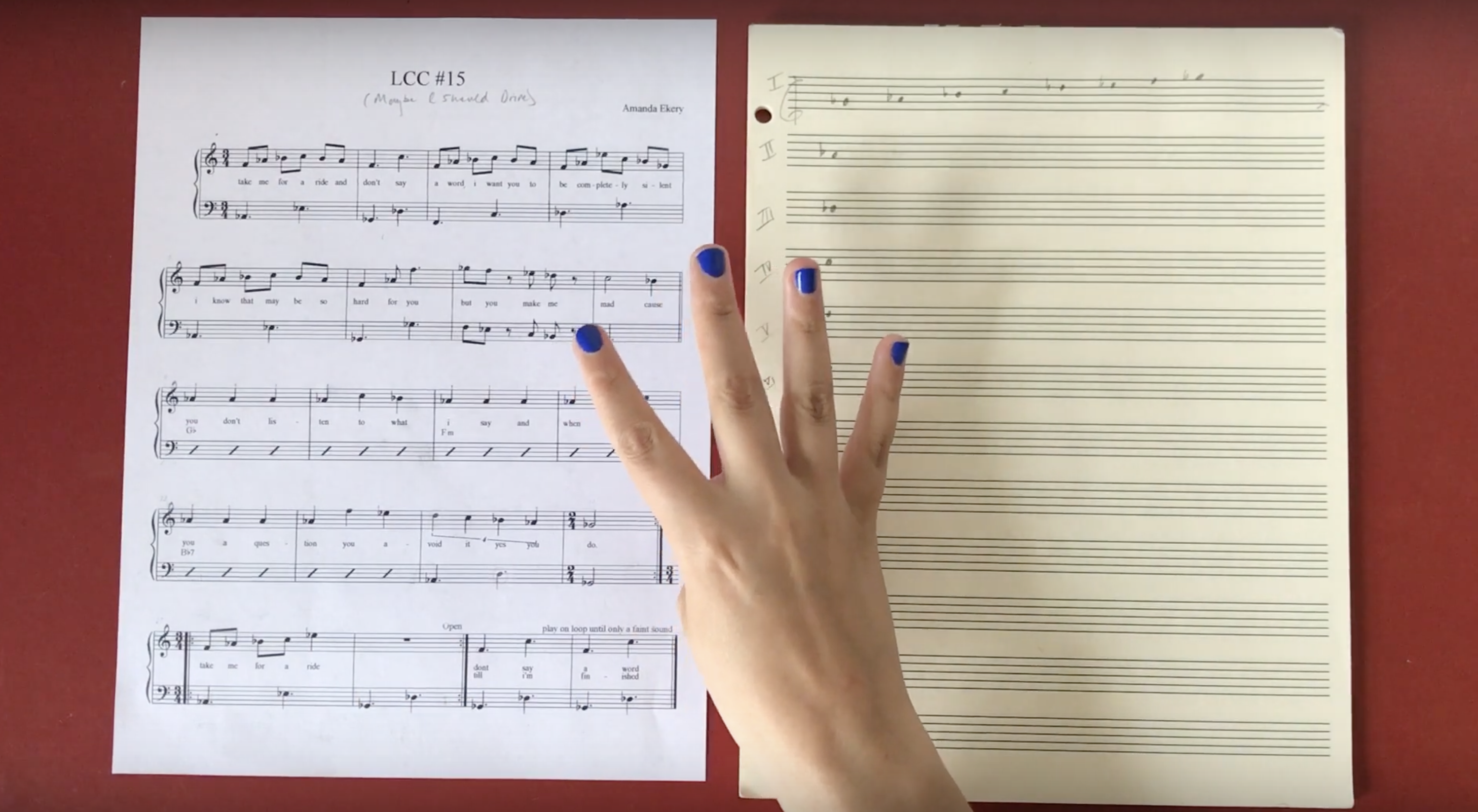 compositional sheet music lays open on a table, a hand with nails painted blue, gestures a four above the music 