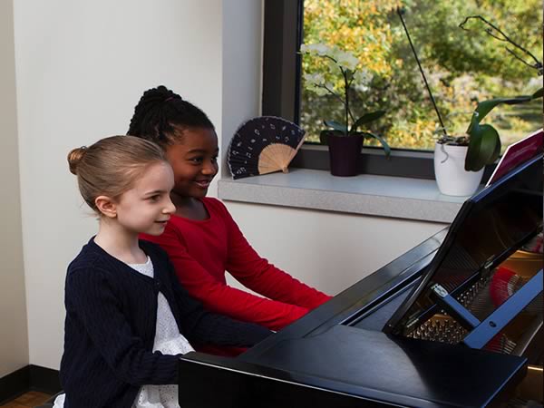 Two smiling girls playing piano at CAA