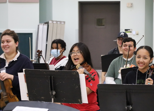 A group of student mariachi violinists smiling and rehearsing together