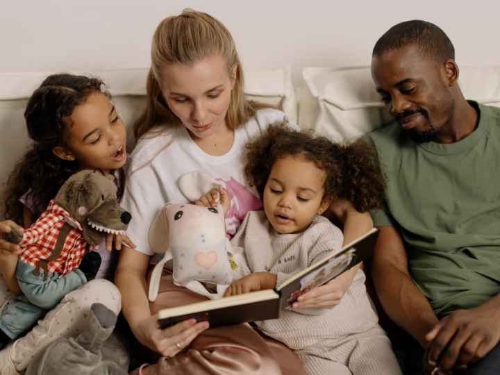 Photo of parents reading book with two young daughters
