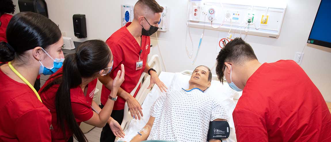 Four nursing students surround a manekin in a hospital bed.