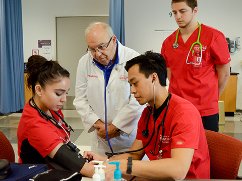 Image of Dr. Kirk with nursing students checking blood pressure