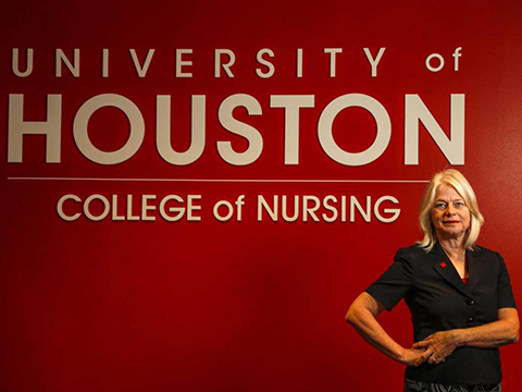 Dean Tart in front of red wall with University of Houston College of Nursing logo in white