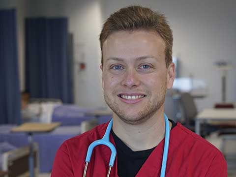 Portrait of a male student smiling in red nursing scrubs.