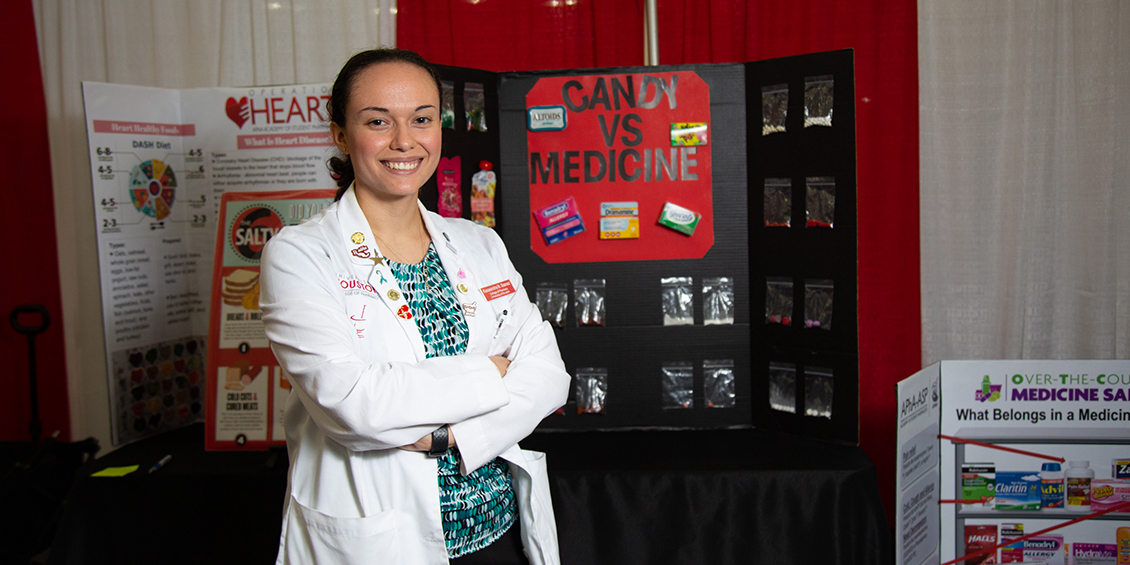 Student stands with presentation board on medicine.