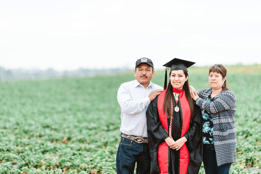 Student in graduation regalia with parent in a crop field