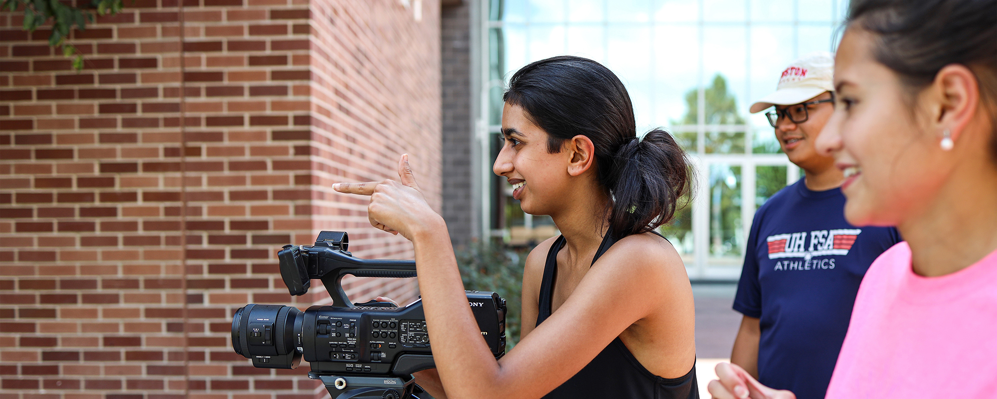 Three students standing behind a video camera facing to the left