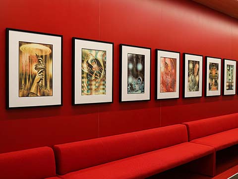 A collection of framed digital photographs on a red wall above red lounge seating