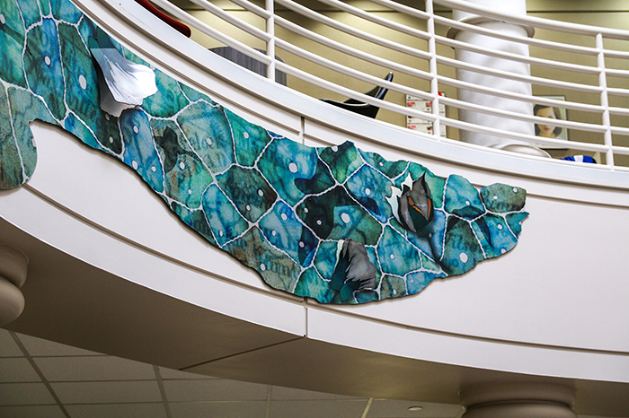 A blue and green metallic panel of cell-like shapes against the wall between two floors in a rotunda