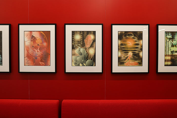 Front view of a collection of framed digital photographs on a red wall above red lounge seating