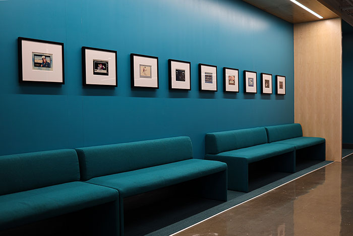 Front view of a collection of framed digital ink prints on a blue wall above blue lounge seating