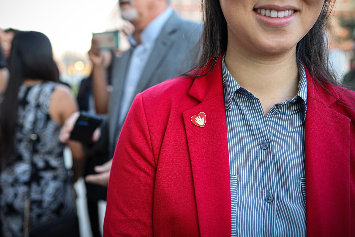 A close up of a student wearing a red jacket and a red heart-shaped lapel pin with an open hand in the middle