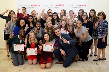 Large group of people doing a university of houston hand gesture standing together in front of a back drop