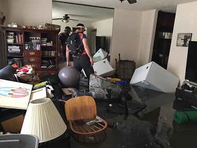 A man wading through a flooded room with furniture, appliances and personal items in the water