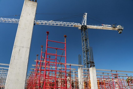A worm's-eye view of a construction crane with cement pillars and red scaffolding in the foreground