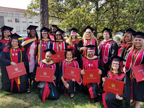 A group of people wearing graduation regalia outside holding red diploma covers
