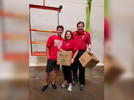 Three people in red shirts stading together holding boxes