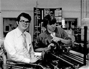Old black and white photo of two men standing by large printing equipment