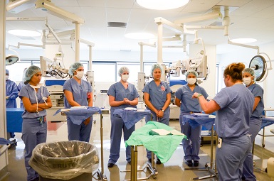 Group of nursing students in scrubs listening to some one presenting in a medical room
