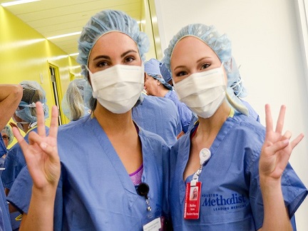 Two female students wearing nurse scrubs with surgical masks and bouffant caps