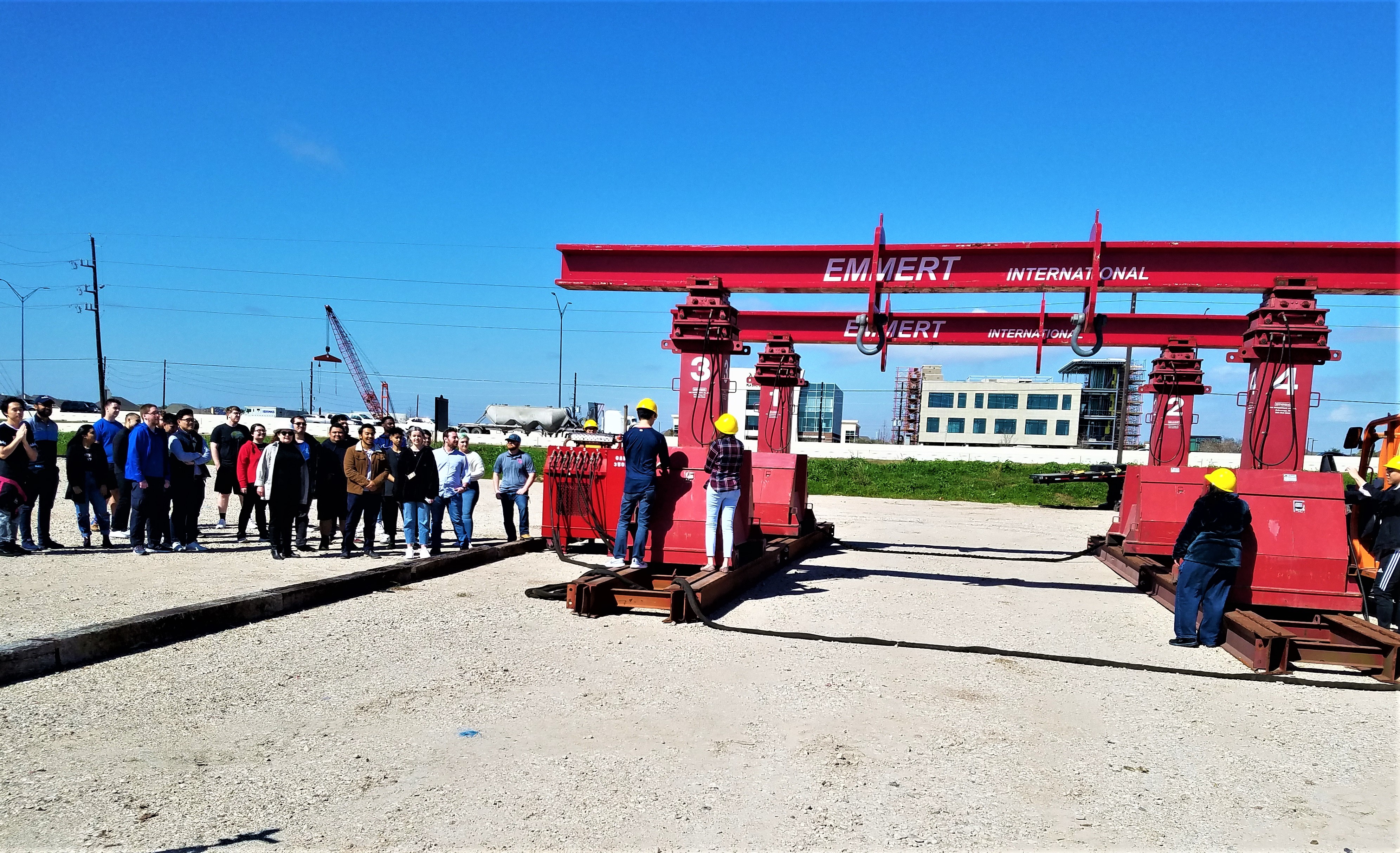 A group of students in business attire stand next to a pair of large red mobile lifts