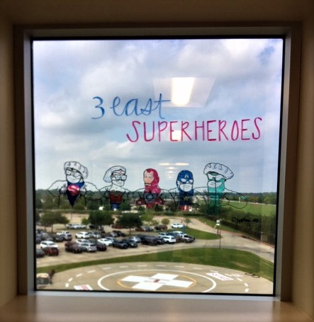 A window with color line drawings of comic book super heroes wearing medical scrubs and outfits