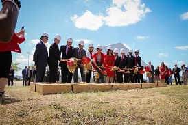 A group of people in suits using shovels to drop dirt into a long wooden box
